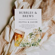 a wedding card with two glasses of beer and flowers on it next to some feathers