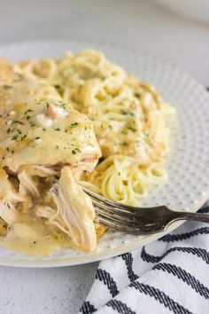 a white plate topped with pasta covered in sauce and chicken breast next to a fork