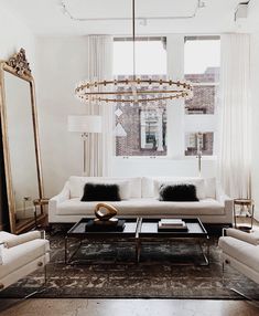 a living room filled with white furniture and a large mirror on the wall above it