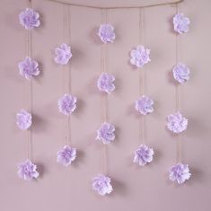 purple paper flowers are hanging from a string on a pink wall in front of a window