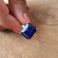 a woman's hand holding a ring with a blue stone in it on top of a wooden table