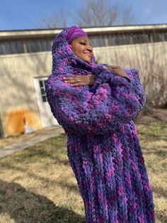 a woman wearing a purple and pink knitted sweater standing in front of a building