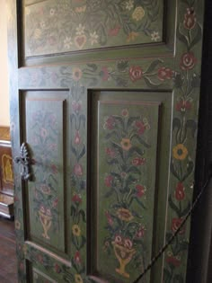 an old green painted cabinet with flowers on it's doors and chain attached to the door