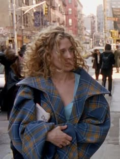 a woman with curly hair walking down the street wearing a blue and yellow plaid coat