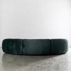 a green velvet couch sitting on top of a cement floor next to a white wall