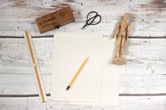 a notepad, pencils and some wooden pegs on a white wood table