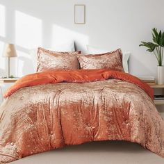 a bed with an orange comforter and two pillows on it in a white room