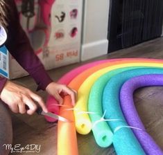 a woman is cutting up some colorful plastic tubes on the floor next to a rainbow - colored tube