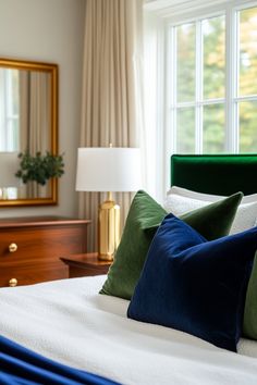 a bed with green and blue pillows in front of a large mirror on the wall