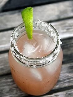 a drink with a lime garnish on the top is sitting on a wooden table