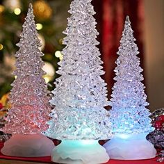 three plastic christmas trees sitting on top of a table next to a tree with lights