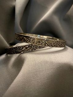 A vintage hand made sterling silver bangles with hand forged floral motif, sold as a set of two. - Total weight: 43.3 grams - Inside diameter: 2 5/8" *Item worn, sold as is* Elegant Ceremonial Sterling Silver Bracelet With Oxidized Finish, Traditional Sterling Silver Bracelet With Intricate Design For Anniversary, Elegant Carved Bangle For Ceremonial Occasions, Etched Sterling Silver Bangle Bracelet For Wedding, Traditional Engraved Sterling Silver Bracelet For Anniversary, Elegant Ceremonial Carved Bangle, Vintage Carved Bangle For Wedding, Ornate Handmade Bangle In Antique Silver, Handmade Ornate Antique Silver Bangle