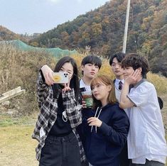 four young people are taking pictures with their cell phones while standing in front of a mountain