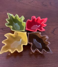 four different colored dishes sitting on top of a wooden table next to an orange, yellow and green leaf