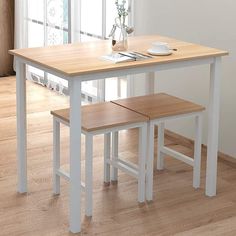 a white table with two benches in front of it on a hard wood floor next to a window