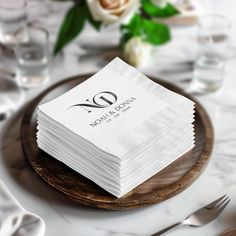 a stack of white napkins sitting on top of a wooden plate next to silverware