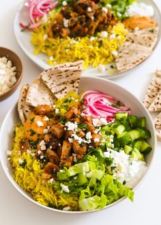 two plates filled with different types of food on top of a white tablecloth next to bowls of rice and pita chips