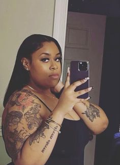 a woman taking a selfie with her cell phone in front of her face and tattoos on her arm