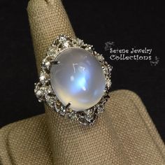 This large rare Moonstone Cabochon Ring is set in 14k solid gold and exhibits mesmerizing blue flash aduralescence. Scintillating diamonds surround this natural beauty!Ring Size: 5.75Total Weight: 13.65 gramsPrecious Metal: 14k solid goldPrecious stones:-Moonstone Center Stone: 18.5mm x 16.2mm, 23.05 carats-White Round Diamond: 0.4ct Fine Jewelry White Gold Moonstone Cabochon Ring, Elegant Multi-stone Moonstone Ring, Wedding Moonstone Cabochon Diamond Ring, Elegant Collectible Moonstone Ring, Unique Diamond Moonstone Ring, Unique Moonstone Diamond Ring, Moonstone Ring With Diamond And Gemstone Accents, Celestial Round Moonstone Ring For Formal Occasions, Unique Oval Moonstone Ring For Formal Occasions