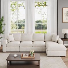 a living room with white couches and two tables in front of large windows that look out onto the yard