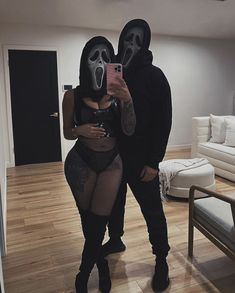 a man and woman wearing masks taking a selfie in a living room with wood floors