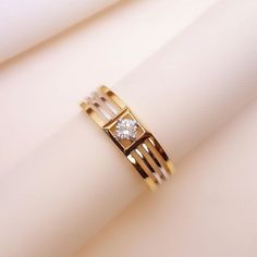 a gold ring with a diamond sitting on top of a white piece of cloth next to it