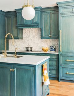 a kitchen with green cabinets and white counter tops, gold faucet hanging from the ceiling