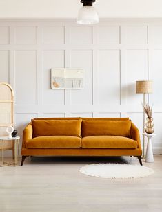 a living room with a couch, chair and lamp on the side table in front of white paneled walls