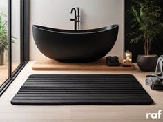 a large black bathtub sitting on top of a wooden floor next to a potted plant