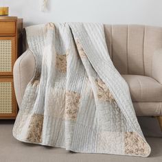 a couch with a blanket on top of it next to a wooden cabinet and lamp