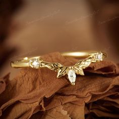 a close up view of a gold ring with leaves and stones on it, sitting on a brown cloth