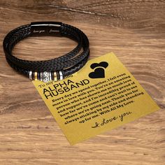 two black leather bracelets sitting on top of a wooden table next to a note