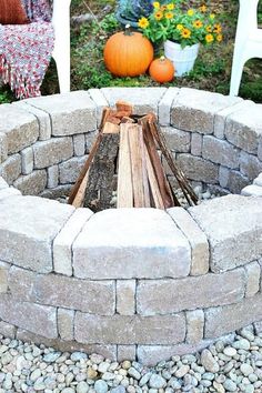 an outdoor fire pit made out of bricks and logs with pumpkins in the background