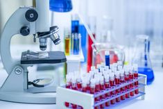 a microscope filled with red liquid in front of some test tubes and flasks