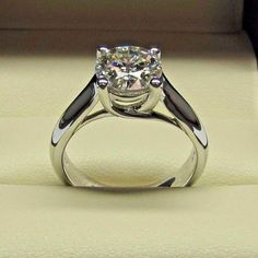 a diamond ring sitting on top of a white cushioned surface with a black stripe around the band