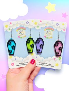 three different colors of earrings are being held up in front of a card with the same design on it