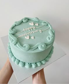 a person holding a cake with the words happy anniversary written on it in white letters