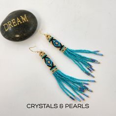 a pair of blue beaded earrings sitting next to a rock with the word dream written on it