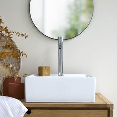 a bathroom sink sitting under a round mirror next to a wooden dresser with plants on it