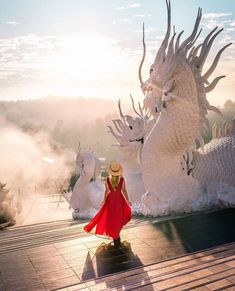 a woman in a red dress and hat standing next to white dragon statues