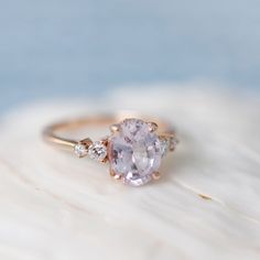 an oval shaped pink sapphire and diamond ring on top of a piece of white coral