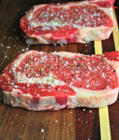 two pieces of raw meat sitting on top of a wooden cutting board with seasoning