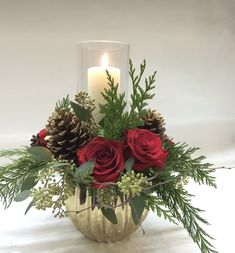 a vase filled with red roses and greenery next to a lit candle on a table