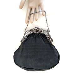 A black handbag with a Dutch 2nd standard silver (.833 purity), repousse frame with windmills, birds, a baby's face, and a cable chain handle.  The interior of the bag is hand sewn, taupe thick gauge, silk satin, and it has two small, side pockets.  The exterior silk is a finely ribbed matte black silk.  The handle drop is 3 1/2 inches, its overall dimensions are 7 1/2 H x 7 1/2 W x 1/2 D inches.  The bag dates from the late 19th to the first half of the 20th century. CONDITION:  Some signs of w Silver Handheld Evening Bag With Chain Strap, Handheld Silver Evening Bag With Chain Strap, Silver Formal Bag With Chain Strap, Elegant Silver Bag With Chain Strap, Classic Silver Bag With Chain Strap, Silver Pouch Shoulder Bag For Evening, Silver Shoulder Bag With Palladium Hardware For Evening, Classic Silver Shoulder Bag For Formal Occasions, Classic Silver Shoulder Bag For Formal Events