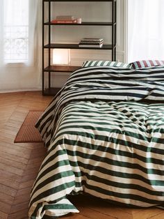 a bed with black and white striped comforter on it next to a book shelf