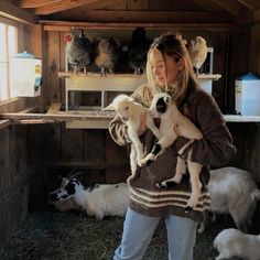 a woman holding two puppies in her arms while standing next to other dogs and chickens