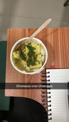 a bowl of food sitting on top of a wooden table next to a notepad