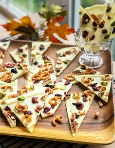 several pieces of cheese with nuts and raisins on a wooden tray next to a glass vase