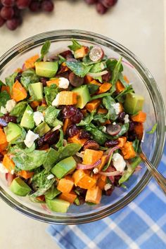 a glass bowl filled with salad on top of a blue and white checkered table cloth