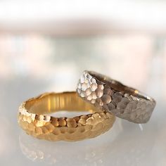 two gold and silver rings sitting on top of a white table next to each other